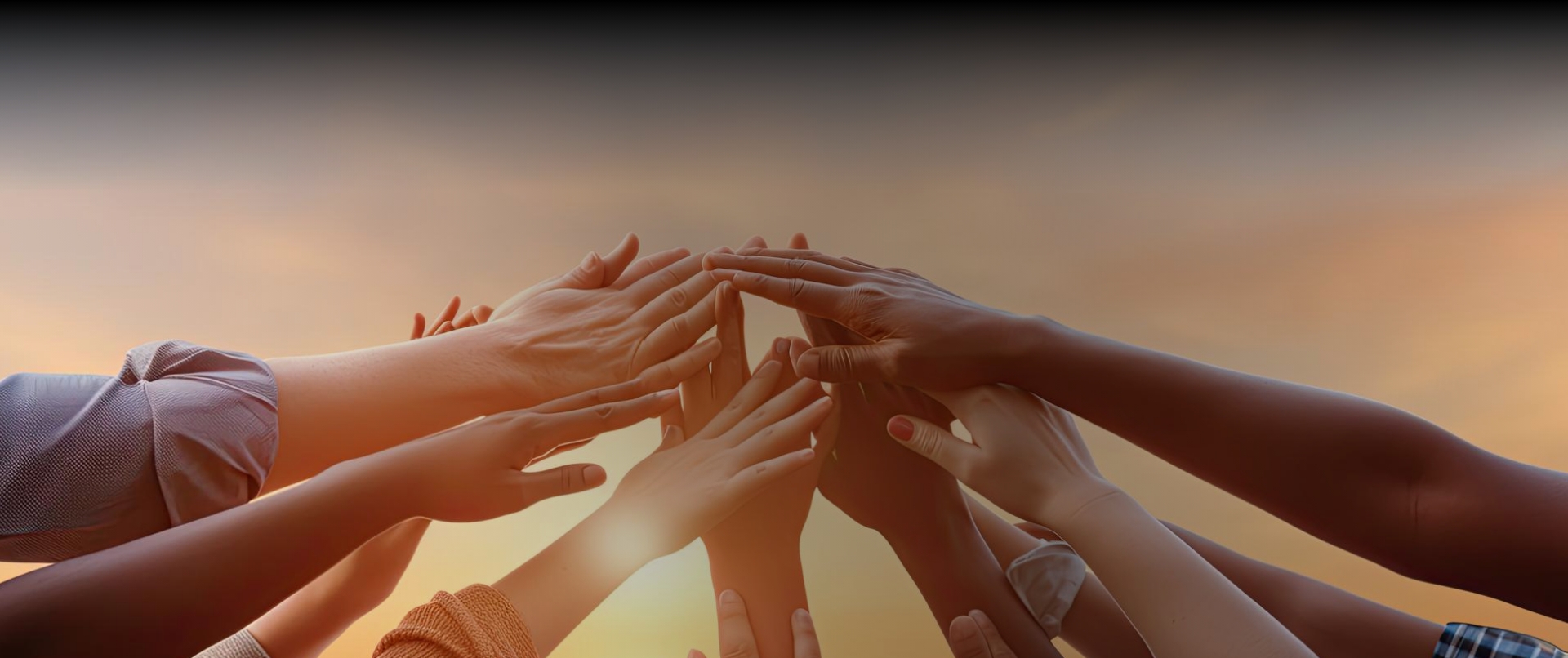 Many hands coming together and reaching upwards against an orange sky background.